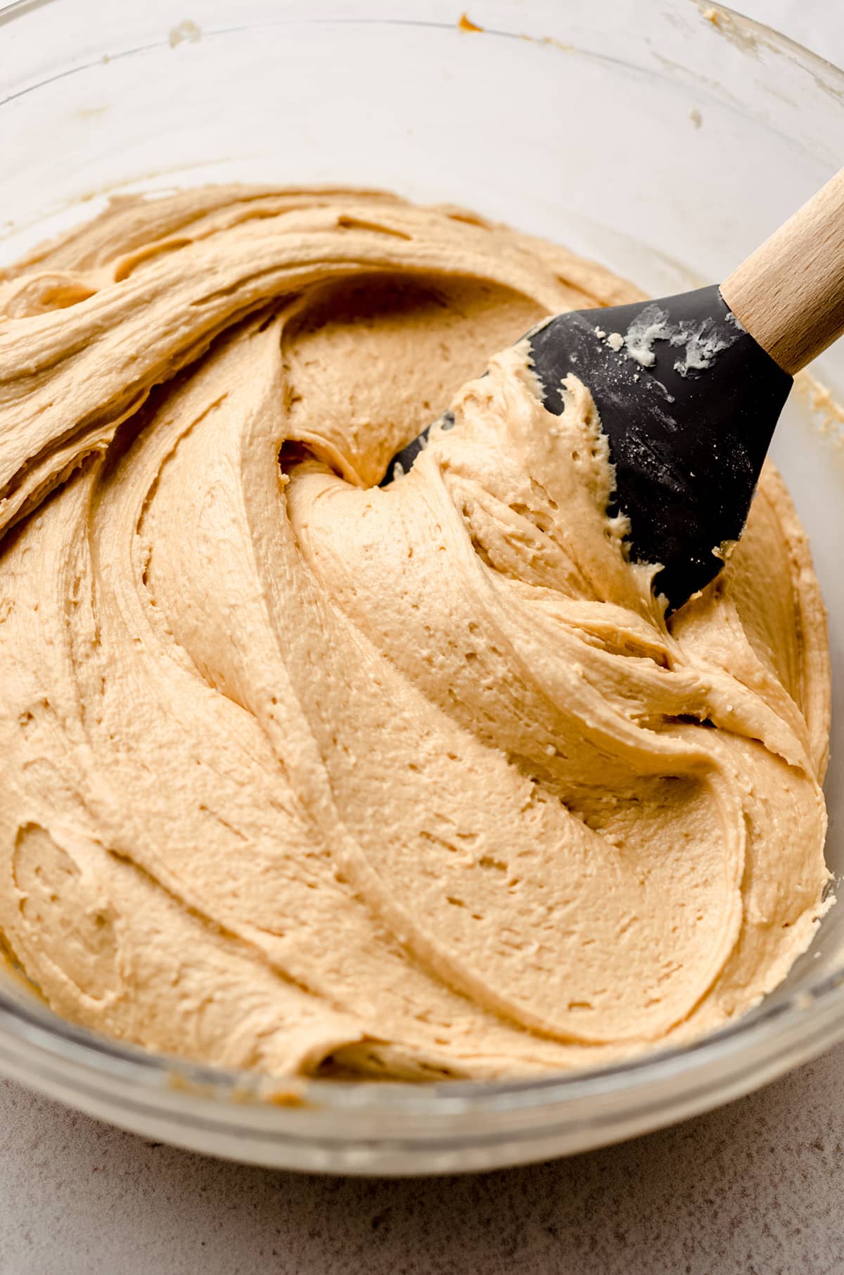 A large bowl of dulce de leche buttercream, being folded together with a silicone spatula.