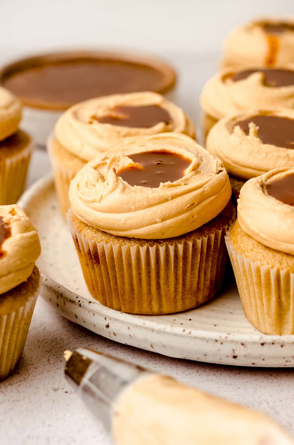 A plate filled with dulce de leche cupcakes, with a piping bag in the foreground.