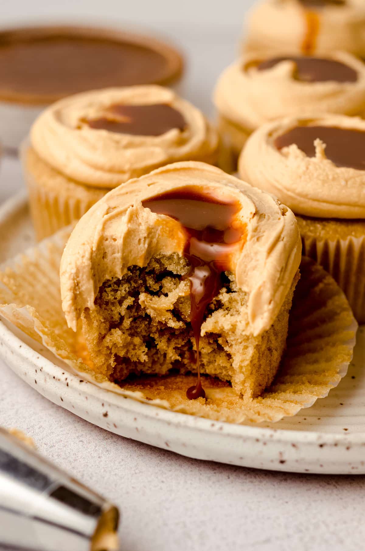 Several dulce de leche cupcakes on a plate, with one with a bite taken out of it.