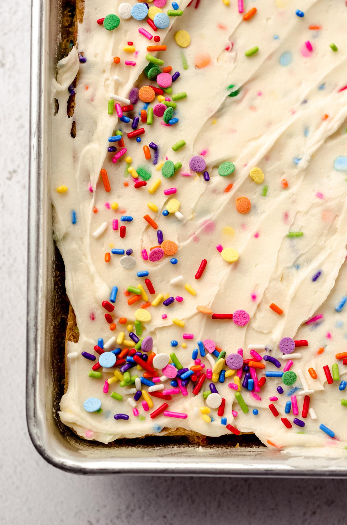An overhead shot of a sheet pan with funfetti cake, topped with sprinkles.
