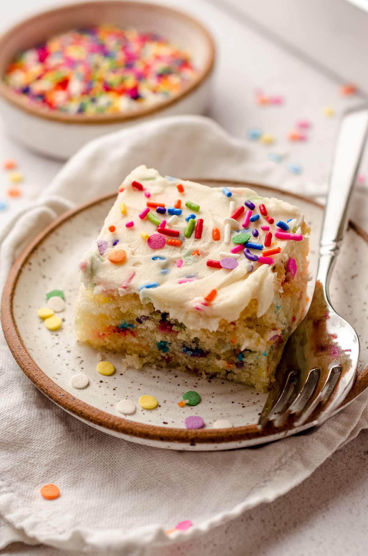 A piece of funfetti cake with vanilla frosting on a plate.