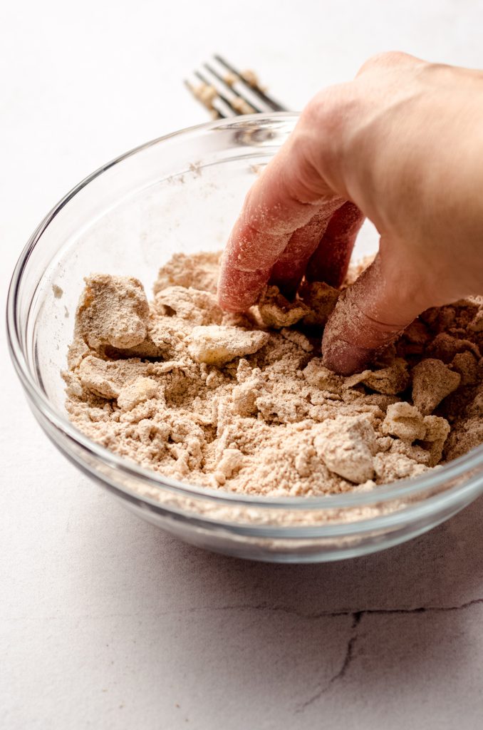 fingers pinching homemade streusel in a bowl