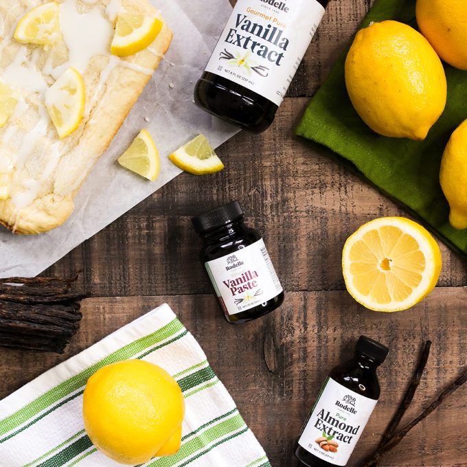Vanilla extract, vanilla paste and almond extract small jars over a wooden surface with lemons.