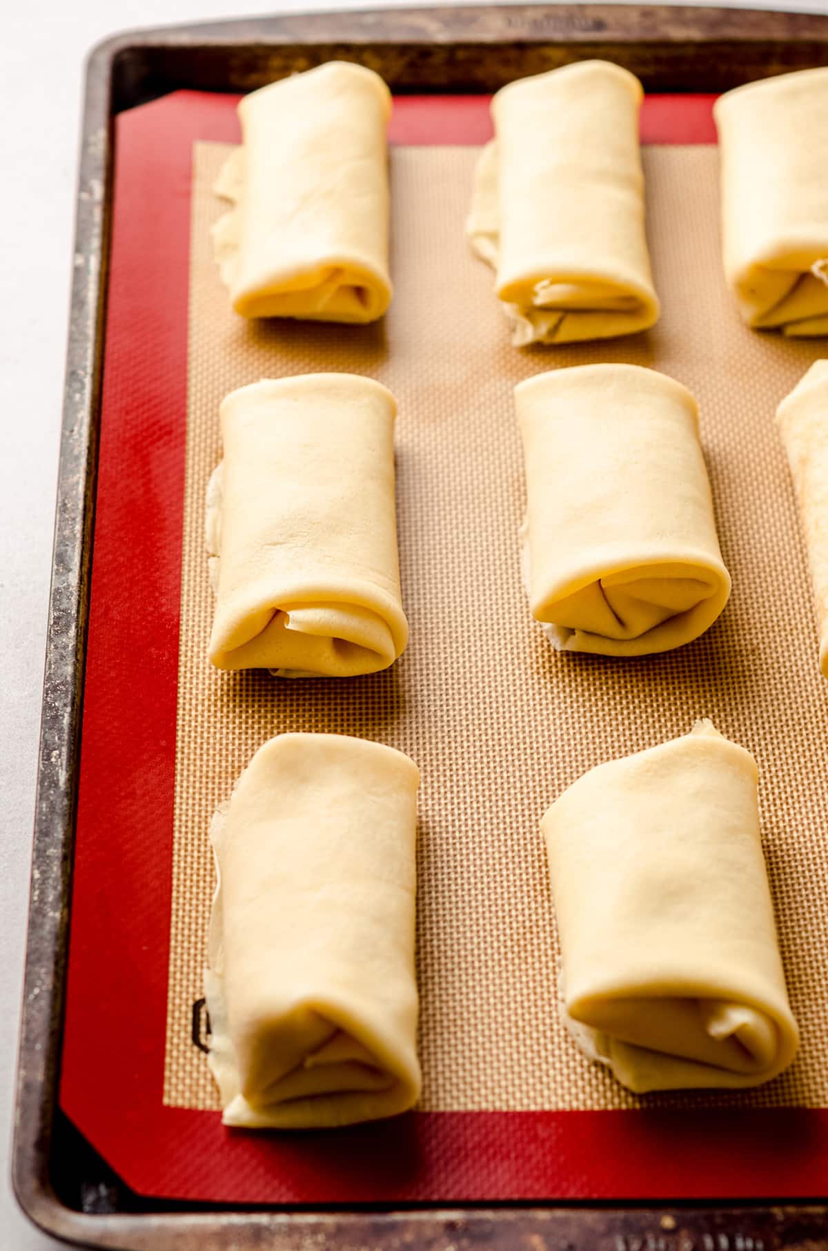 Cheese blintzes rolled and placed on a silicone parchment lined baking sheet.