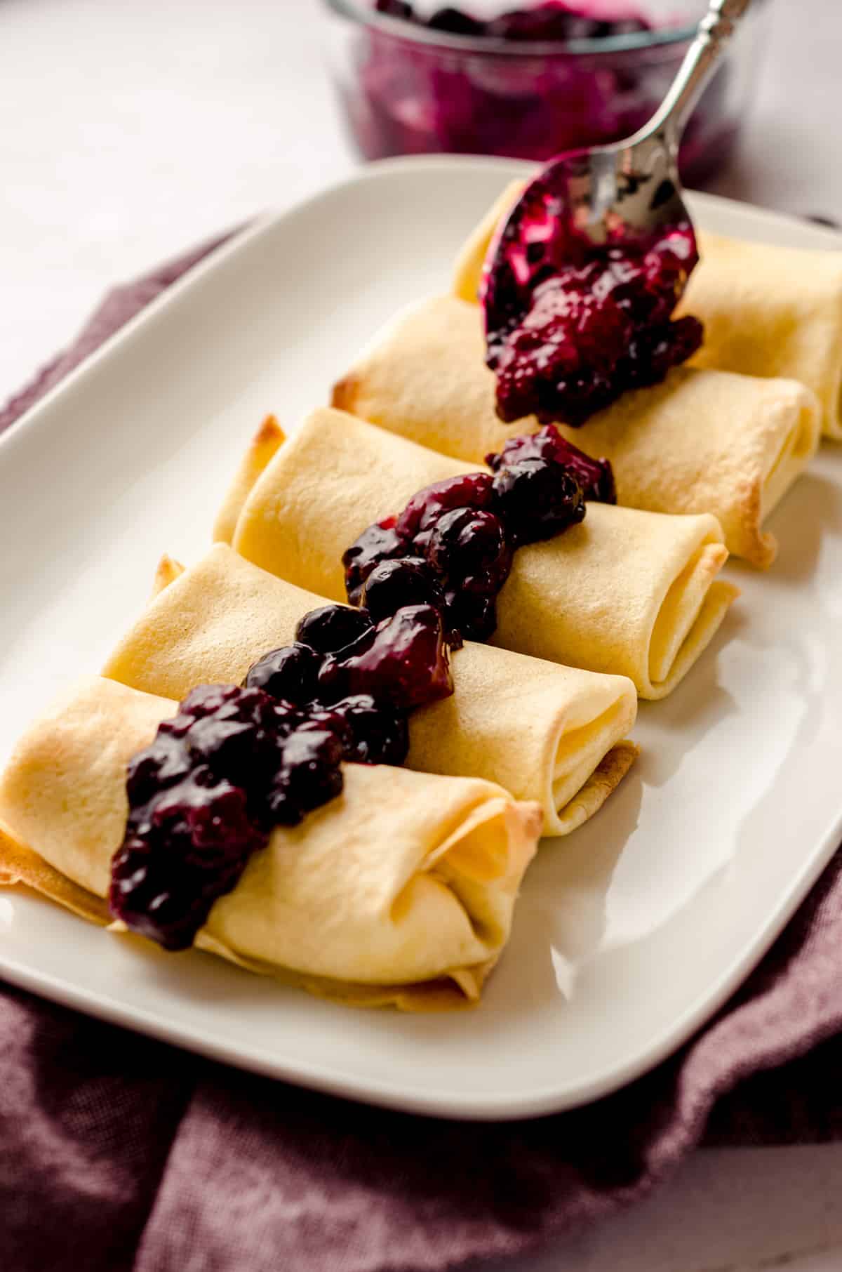 Spooning berry compote over a platter of cheese blintzes.