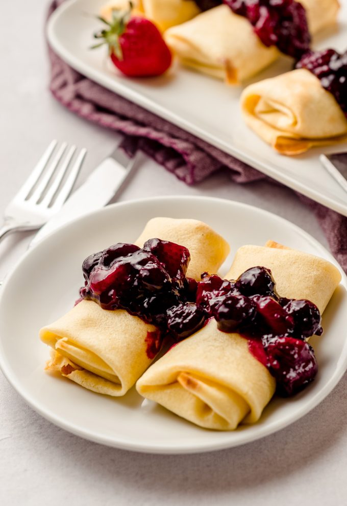 Two cheese blintzes on a plate, topped with a berry compote.