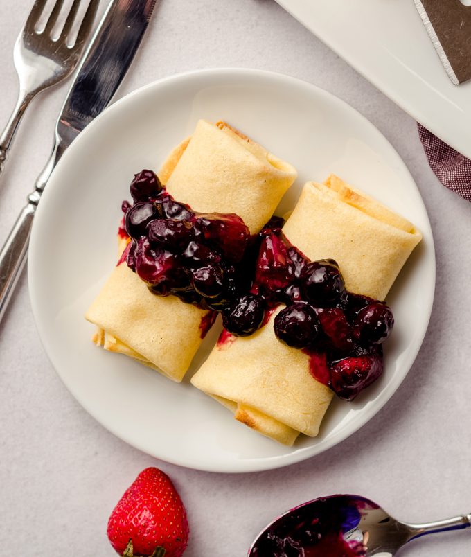 Rolled cheese blintzes that have been topped with berry compote.