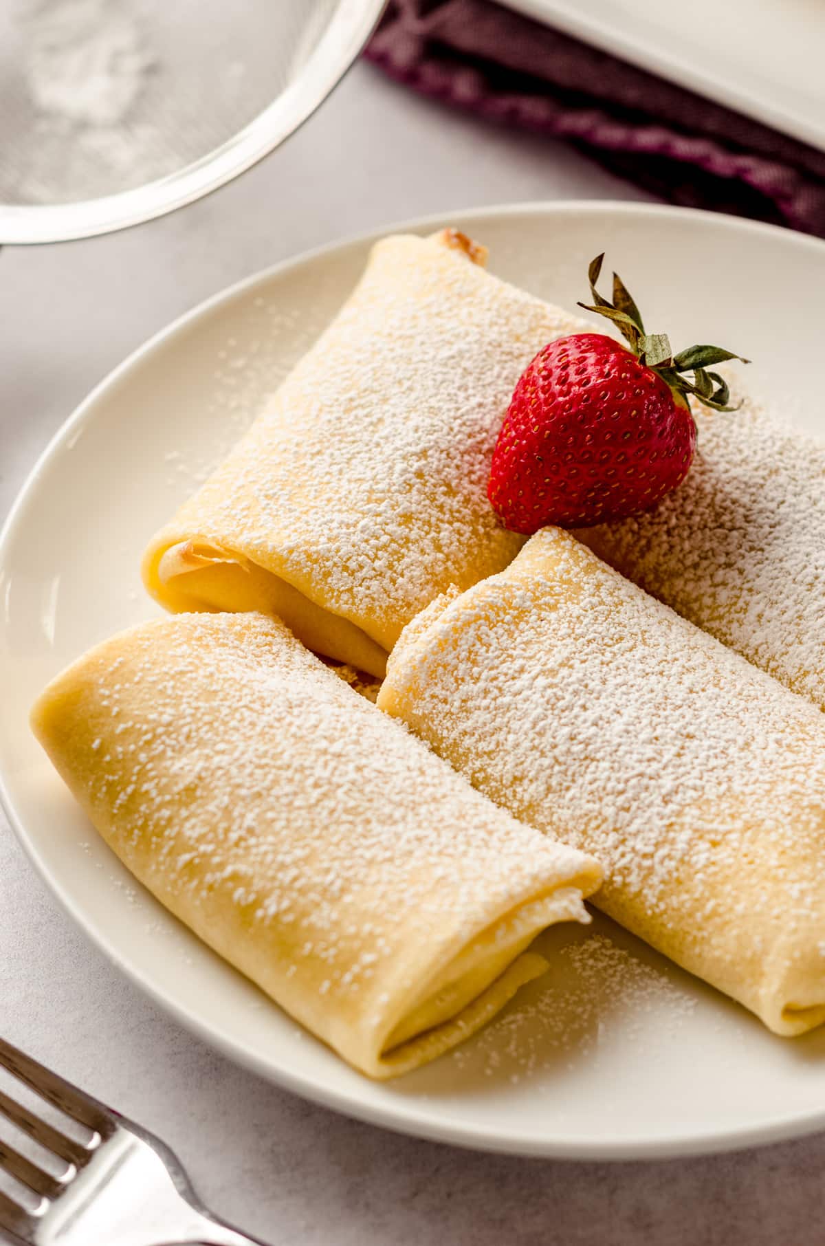 Three cheese blintzes on a plate, garnished with a single strawberry.