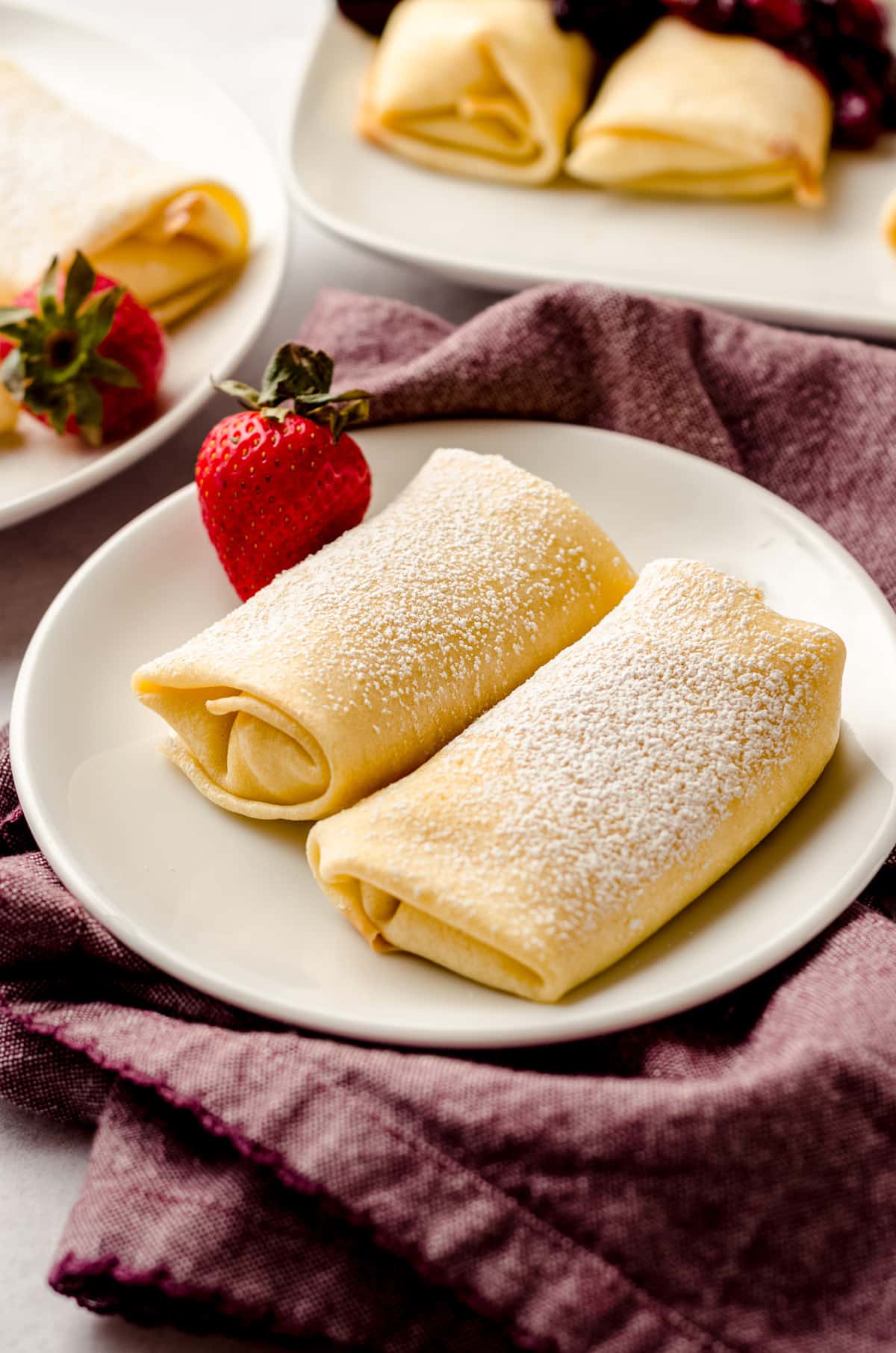 Rolled blintzes on a white plate, garnished with a strawberry.