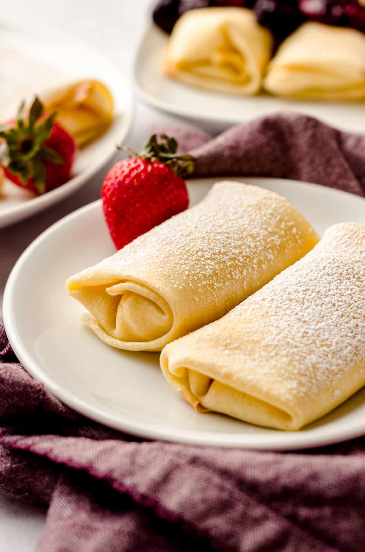 Two rolled cheese blintzes, garnished with a strawberry.