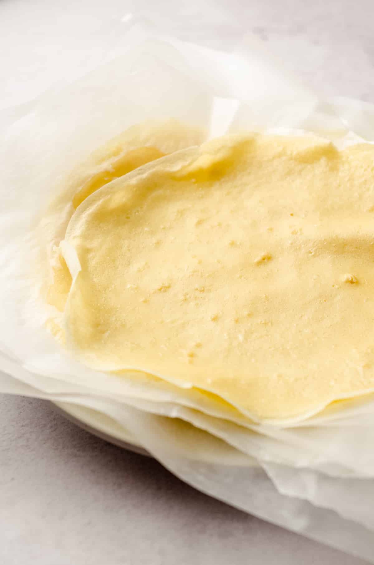 Crepes stacked on a plate between layers of parchment paper.