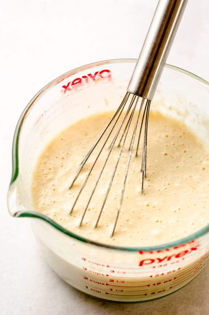 A large glass measuring cup with a crepe batter inside, being whisked.