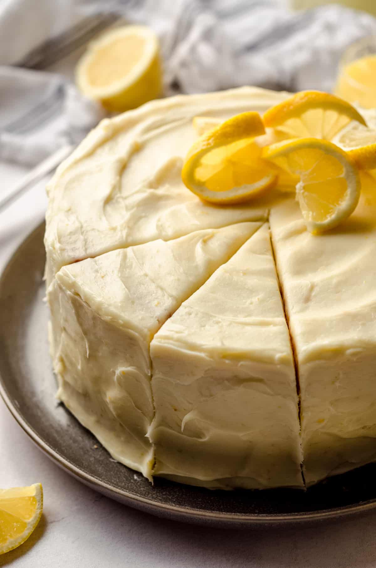 A lemon cake decorated with lemon slices and cut into wedges.