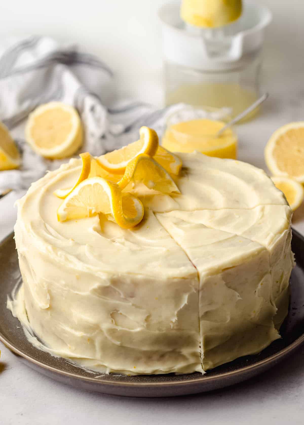 A large lemon cake decorated with lemon slices, with small wedges scored.