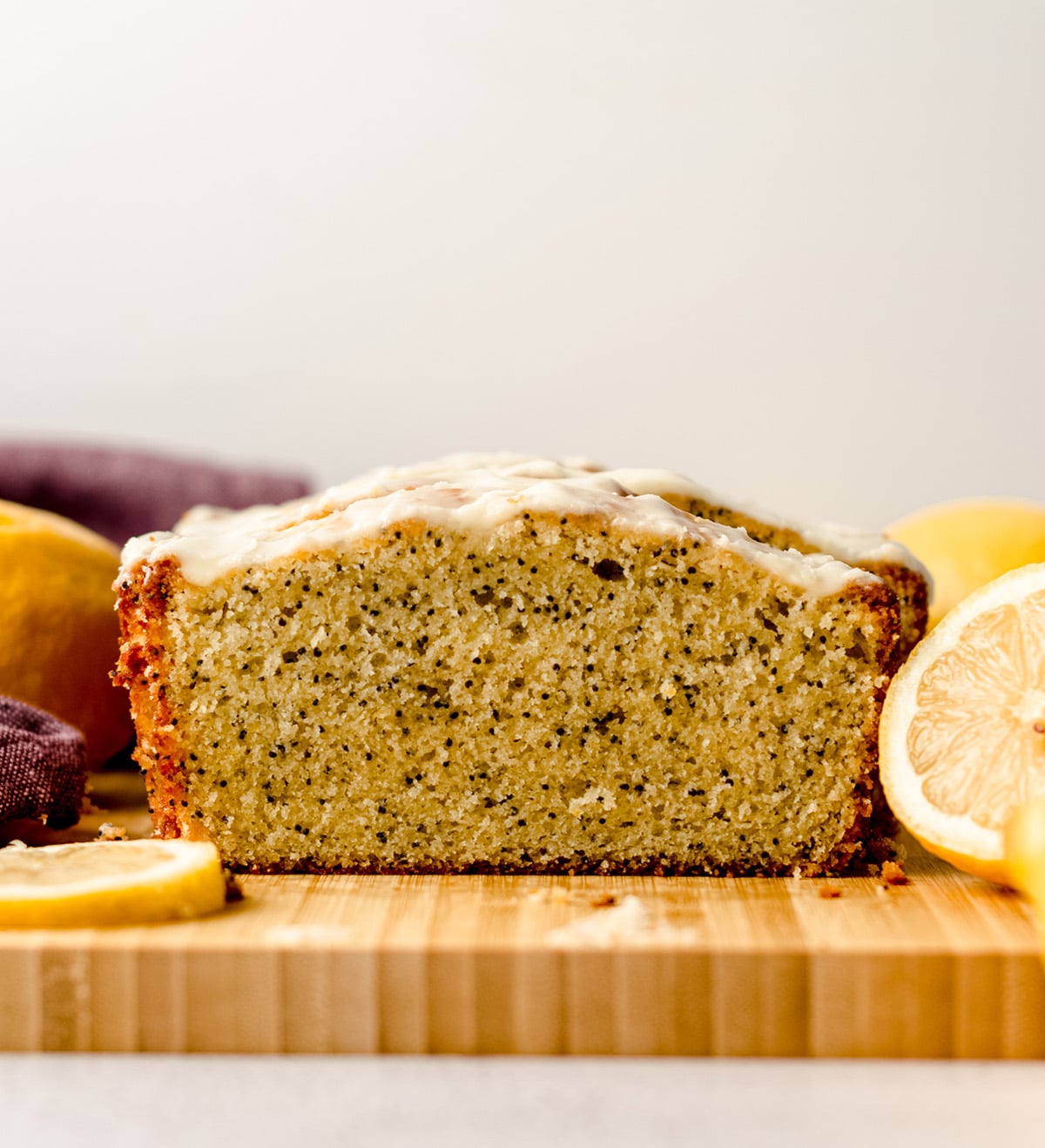 A front view of a loaf of lemon poppy seed bread on a cutting board, topped with glaze.