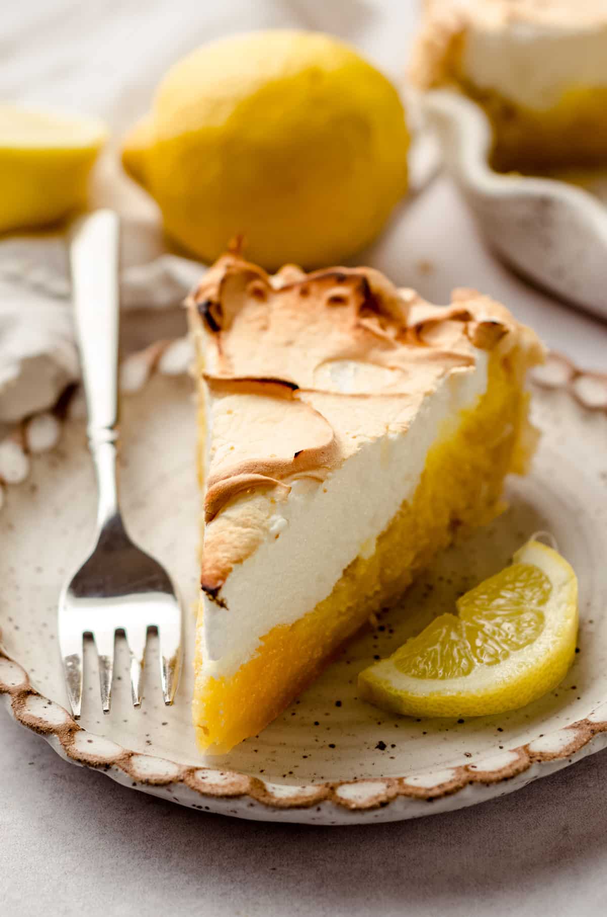 A slice of lemon meringue pie with lemons as garnish.