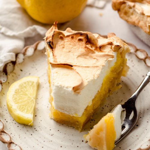 A slice of lemon meringue pie with a piece taken out with a fork.