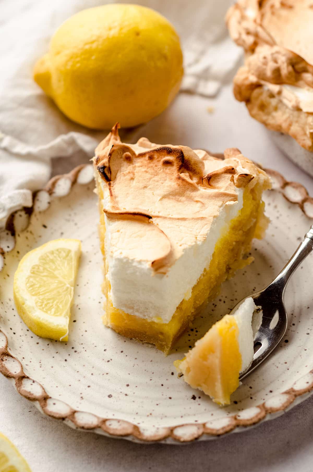 A slice of lemon meringue pie with a piece taken out with a fork.