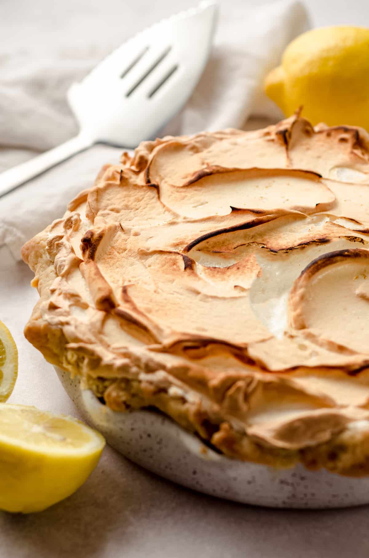 A baked lemon meringue pie, with browned meringue and lemons in the background.