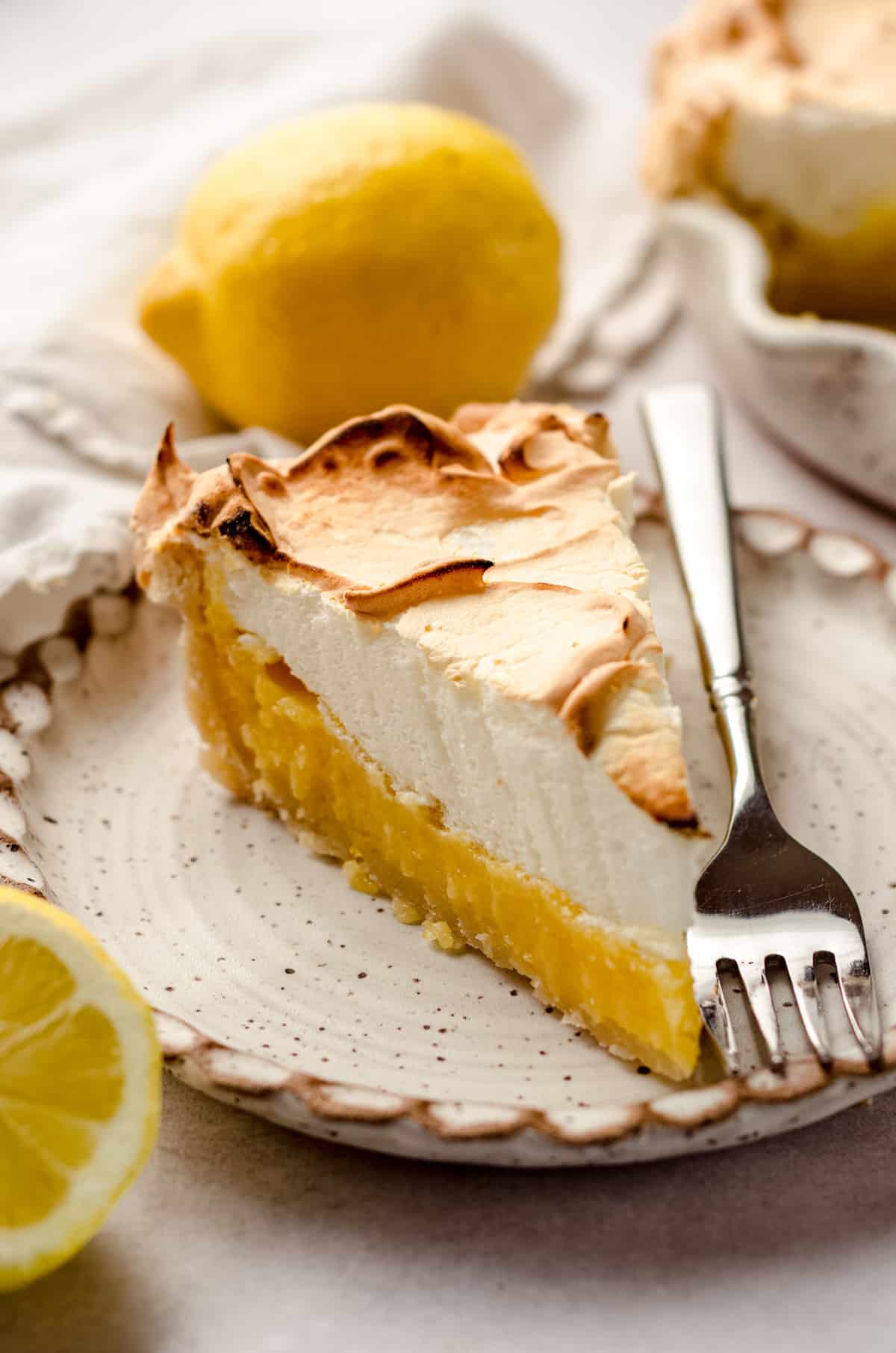 A slice ofThis classic lemon meringue pie recipe features a sweet and tart homemade lemon curd filling and a light and fluffy meringue topping. Bake this lemon meringue pie in the oven to insure the filling sets and creates a beautiful and impressive dessert with clear, sturdy, defined layers. lemon meringue pie on a plate, with a fork on the side.