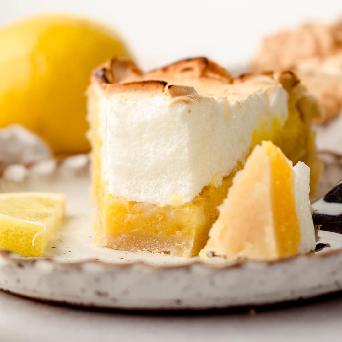 A slice of lemon meringue pie on a plate, with a small portion removed with a fork.