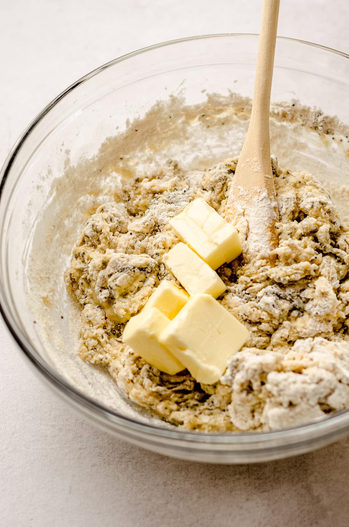 Adding softened butter to a bowl of sweet roll batter with poppy seeds.