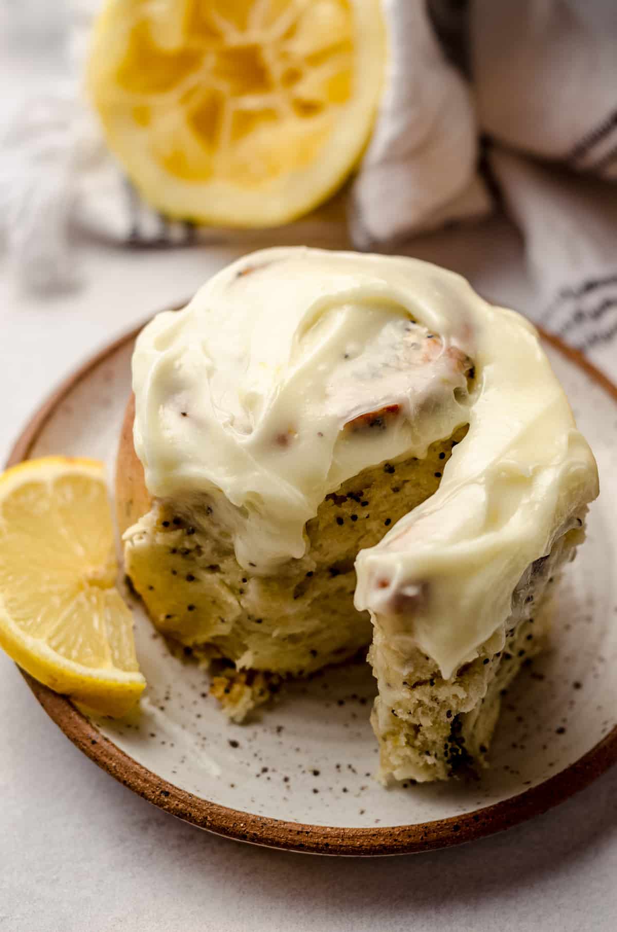 A lemon poppy seed roll on a plate, topped with cream cheese frosting.