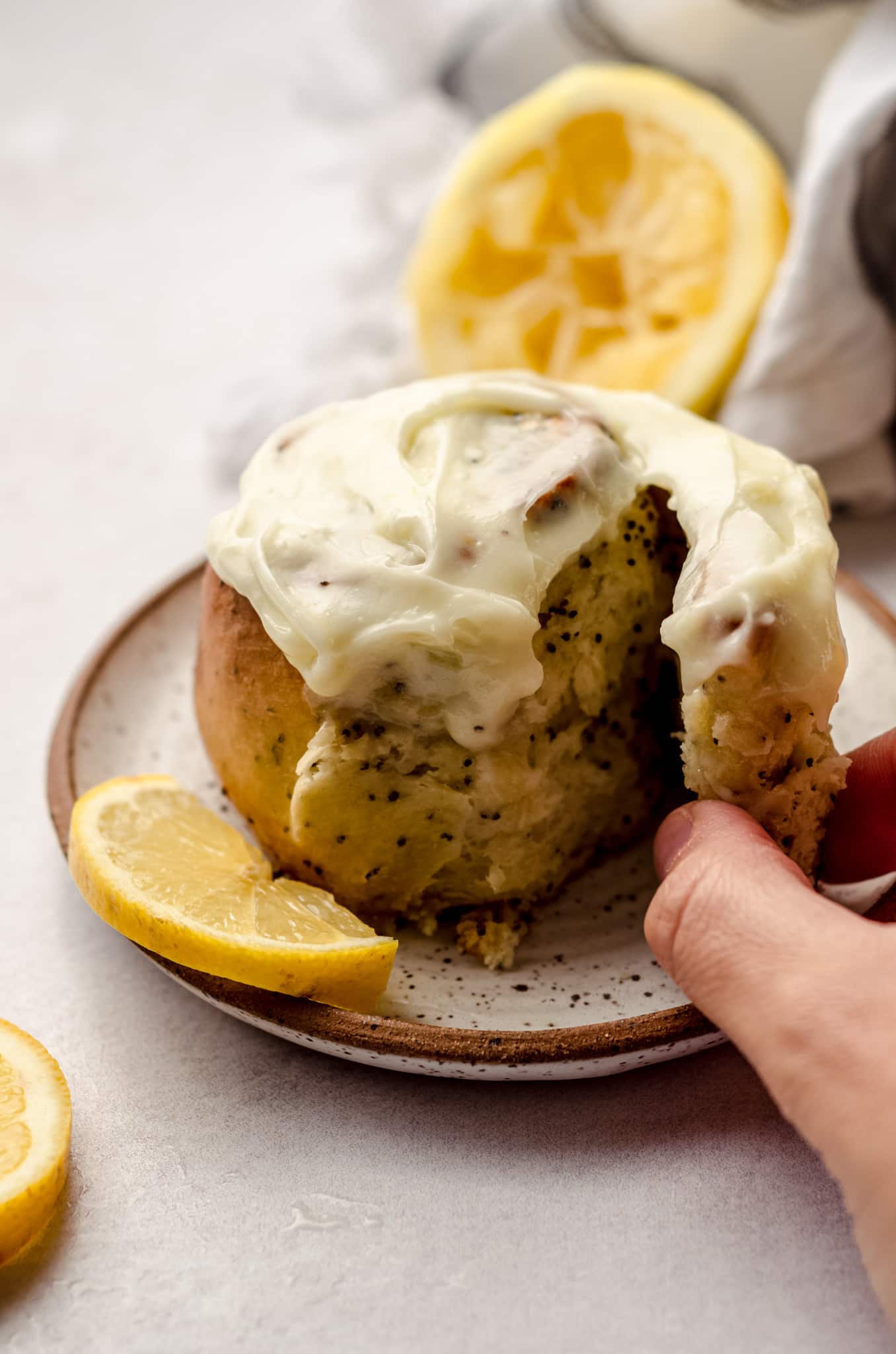 A hand reaching in to take apart a lemon poppy seed swirl roll with cream cheese frosting.