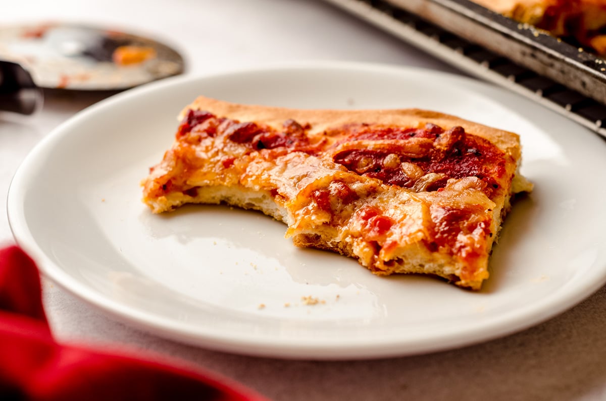 slice of homemade pizza on a plate with bites taken out of it