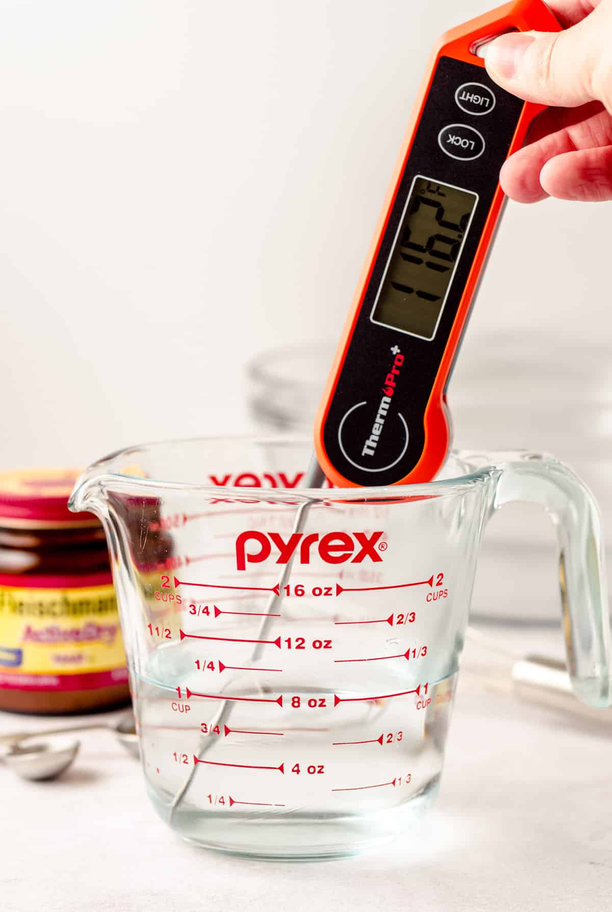 an instant read thermometer testing the temperature of water in a glass measuring cup