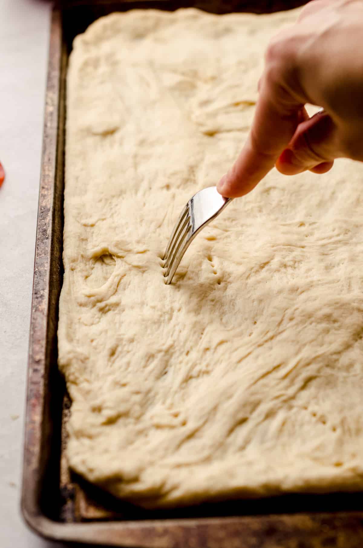 Pricking the surface of a pizza dough, fitted into the sheet pan.