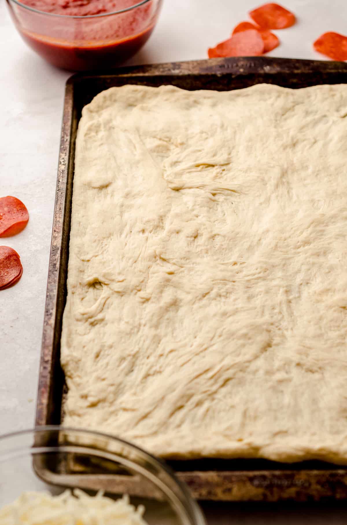 A sheet pan filled with stretched homemade pizza dough.