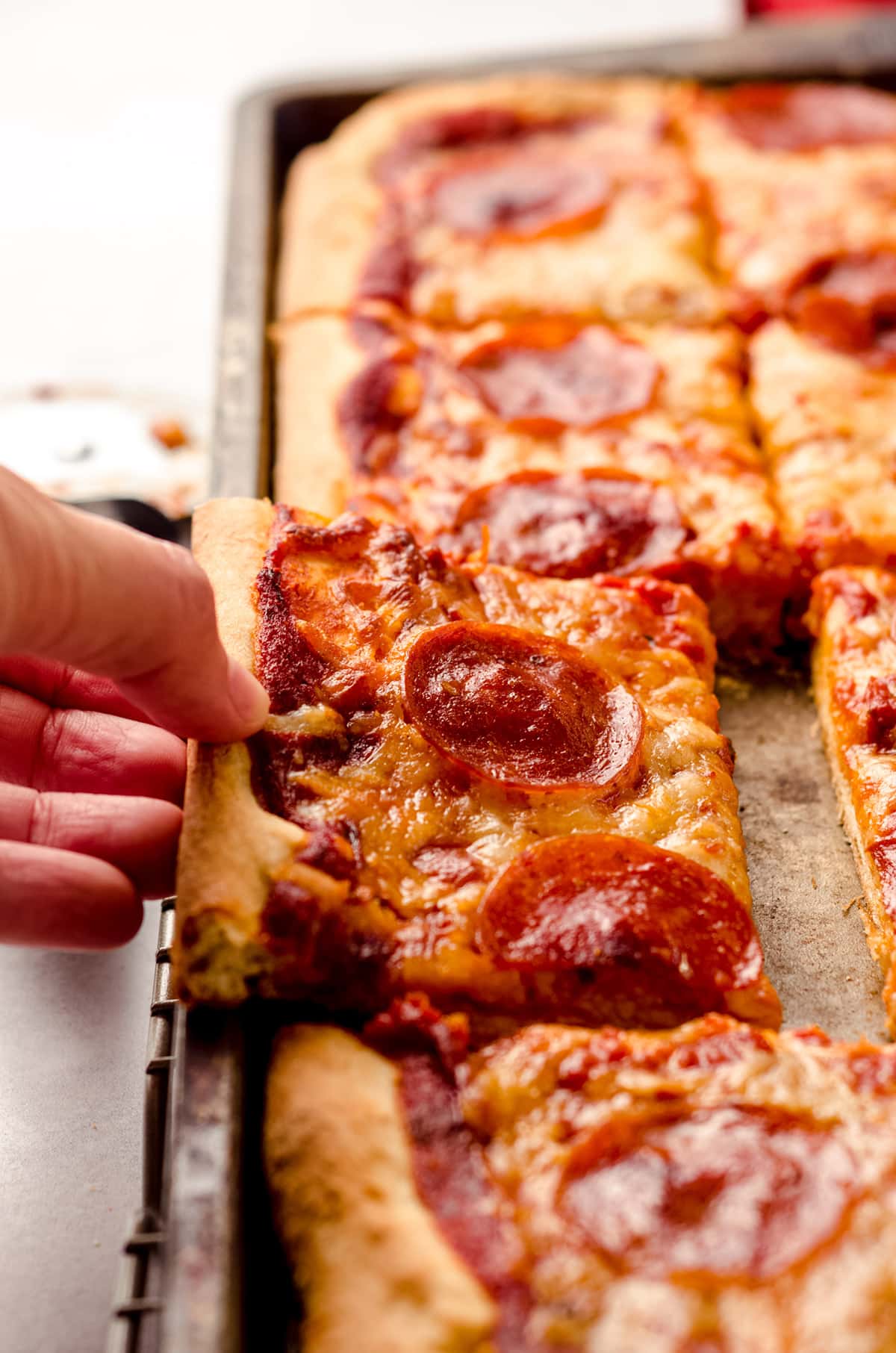 A hand removing a portion of pizza from a sheet pan.