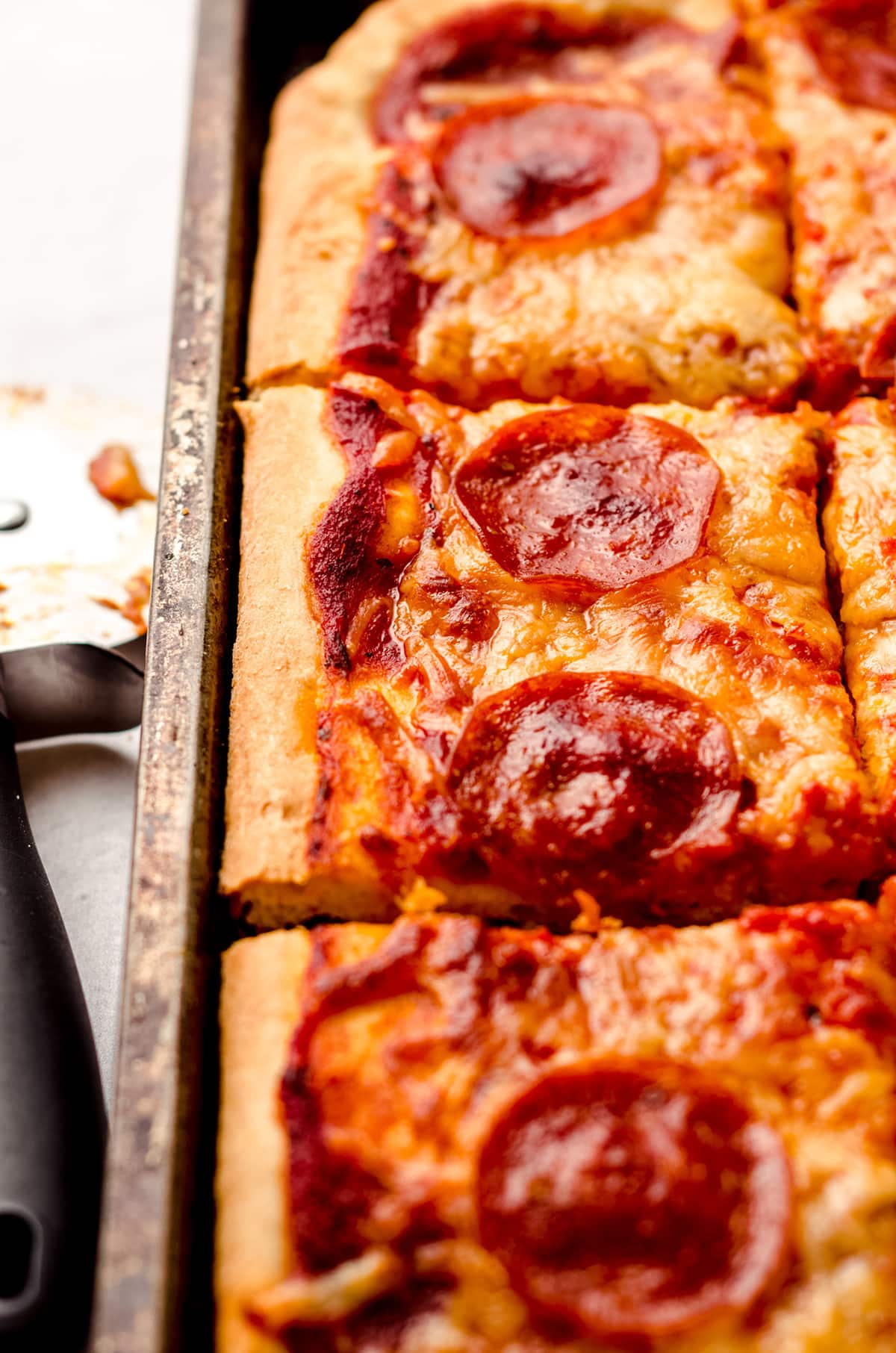 A large square cut pizza, baked in a sheet pan and topped with pepperoni.
