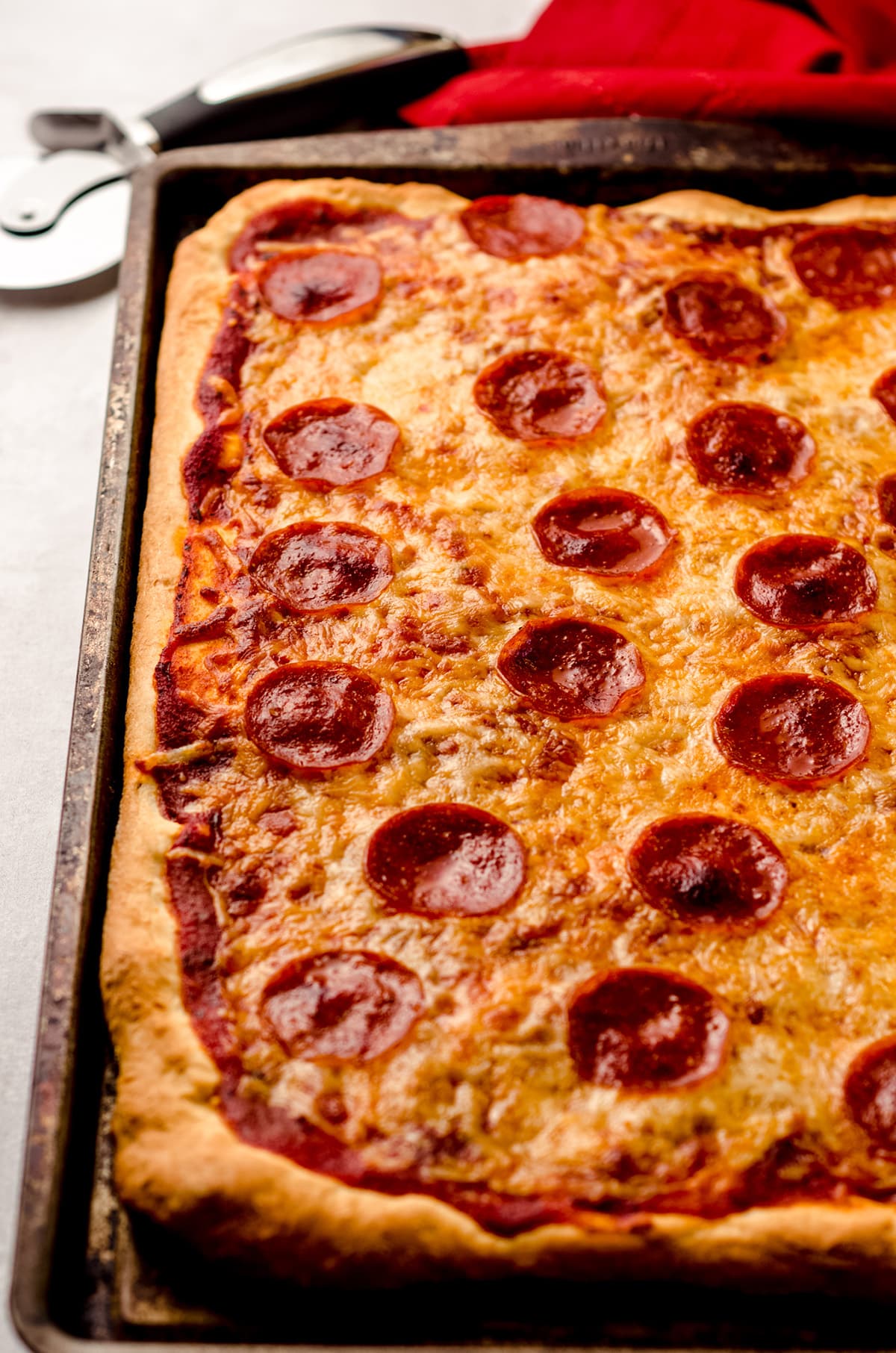 A fully baked rectangle pizza, topped with cheese and pepperoni.