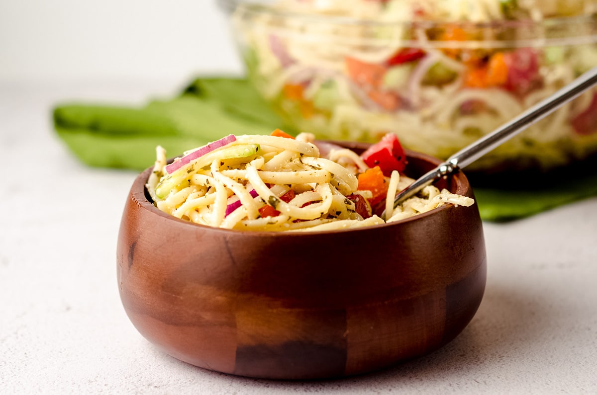 A small bowl of easy spaghetti salad, with a serving bowl in the background.