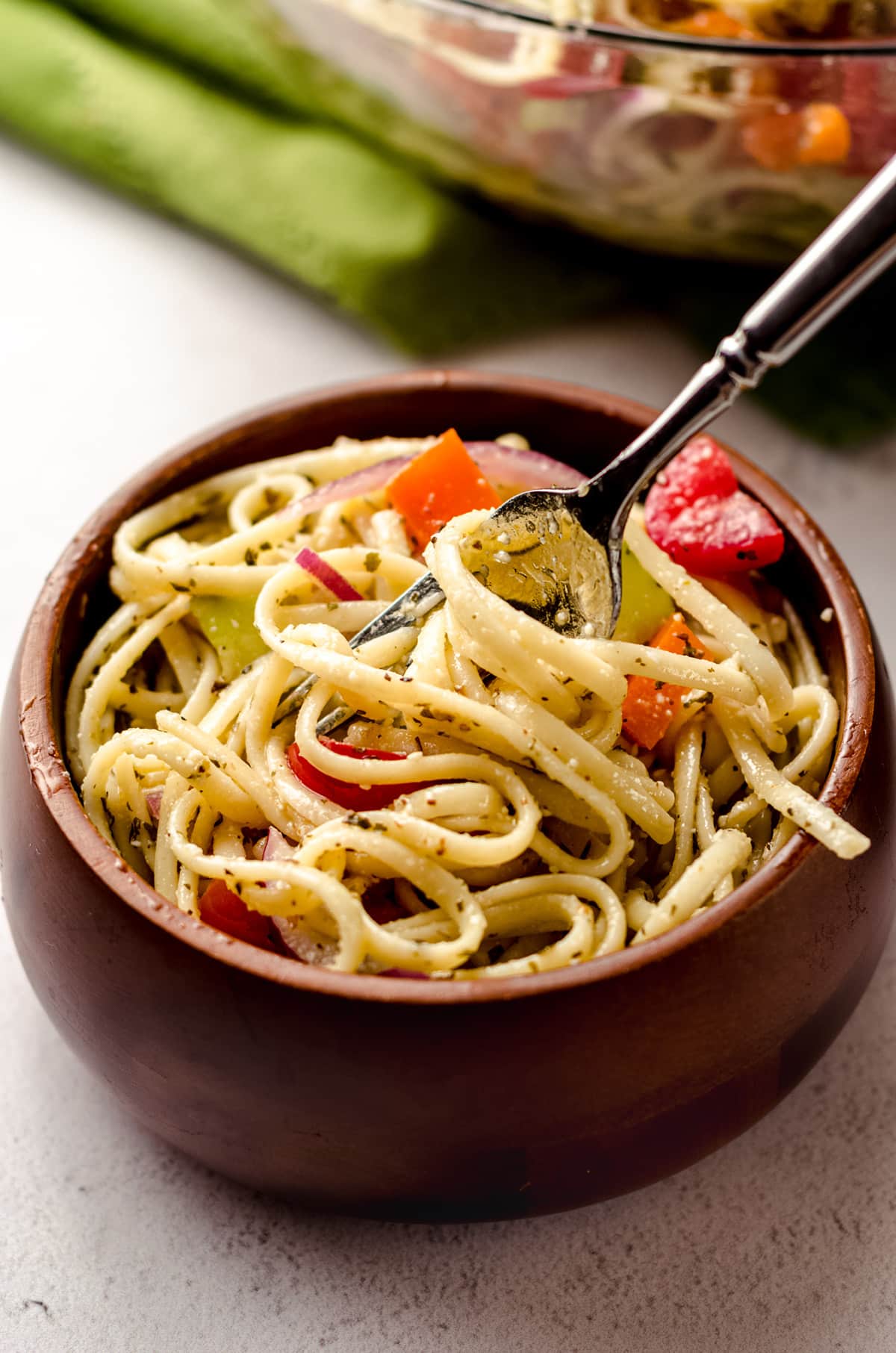 A fork twirling some cold spaghetti noodles in a bowl.