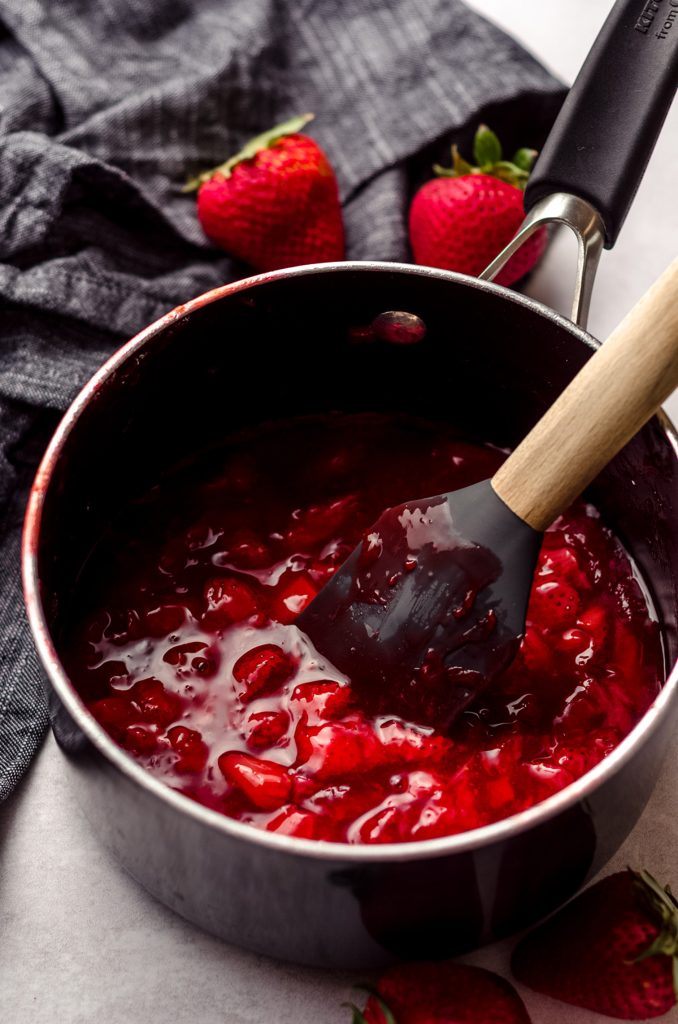 saucepan full of homemade strawberry compote with a silicone spatula