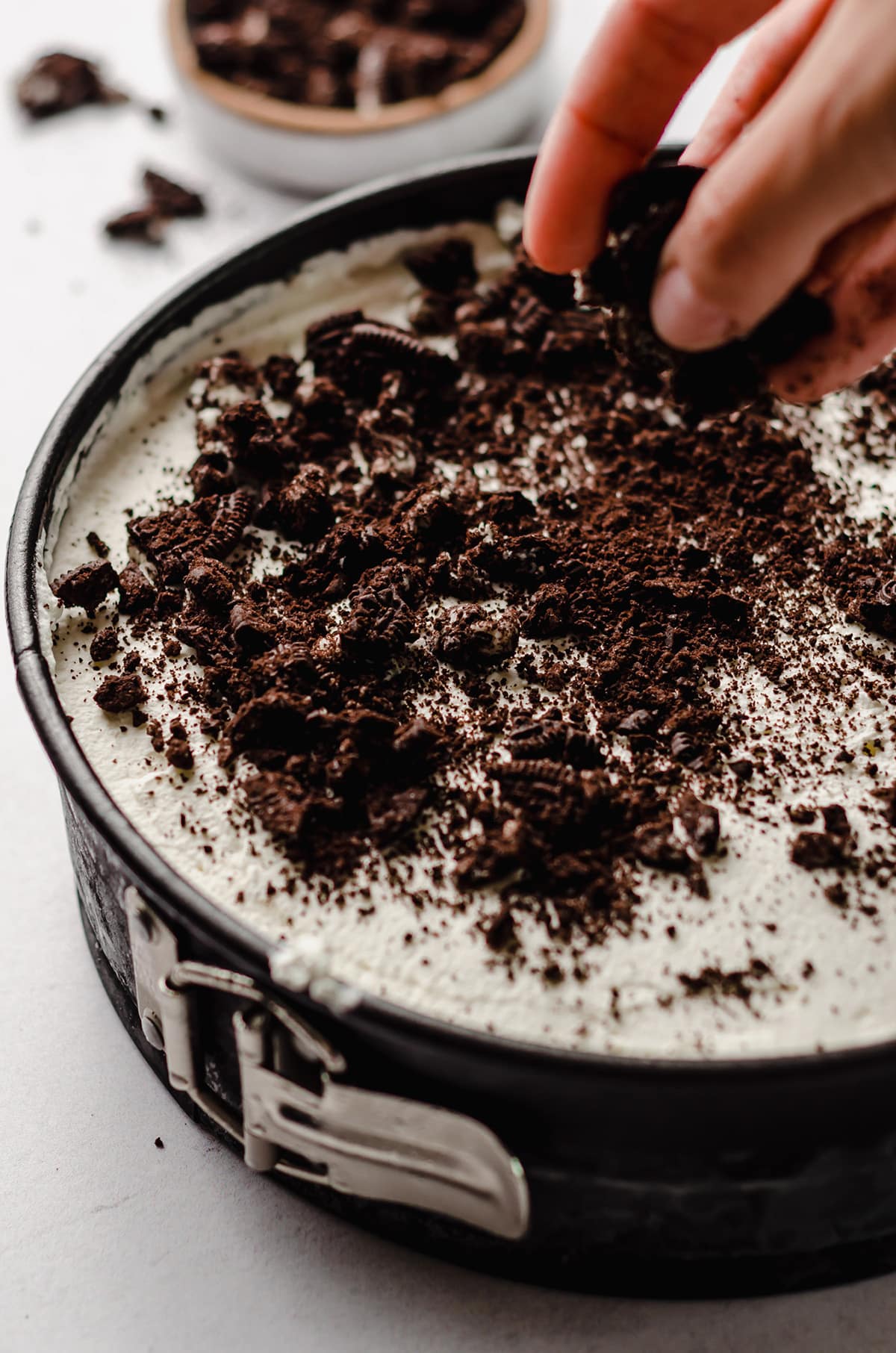 Sprinkling Oreo cookie crumbs on top of an ice cream cake.
