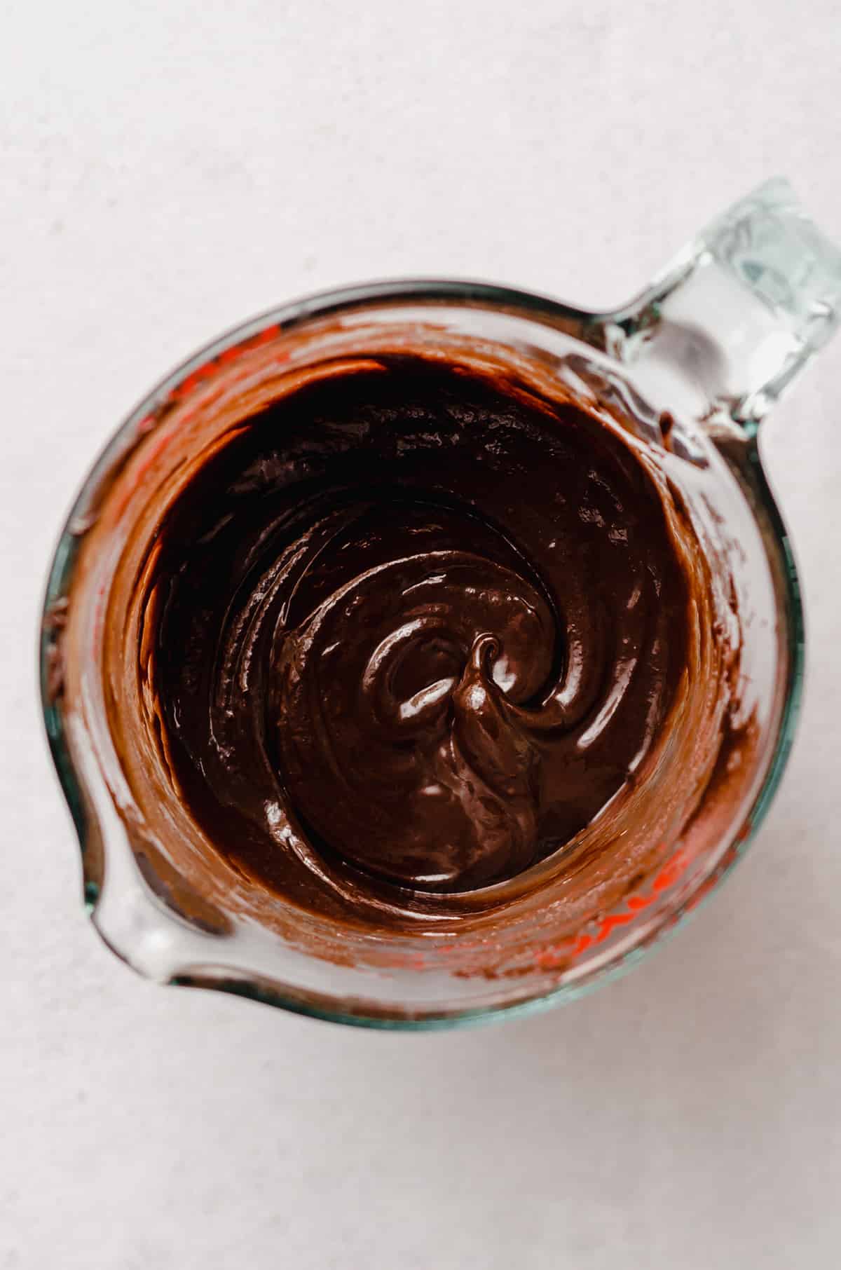 A measuring cup of warmed hot fudge sauce.