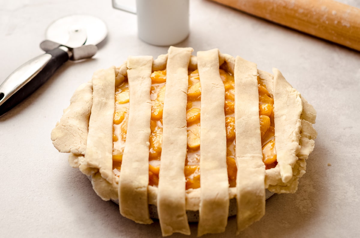 Laying strips of pie dough over a fruit pie.