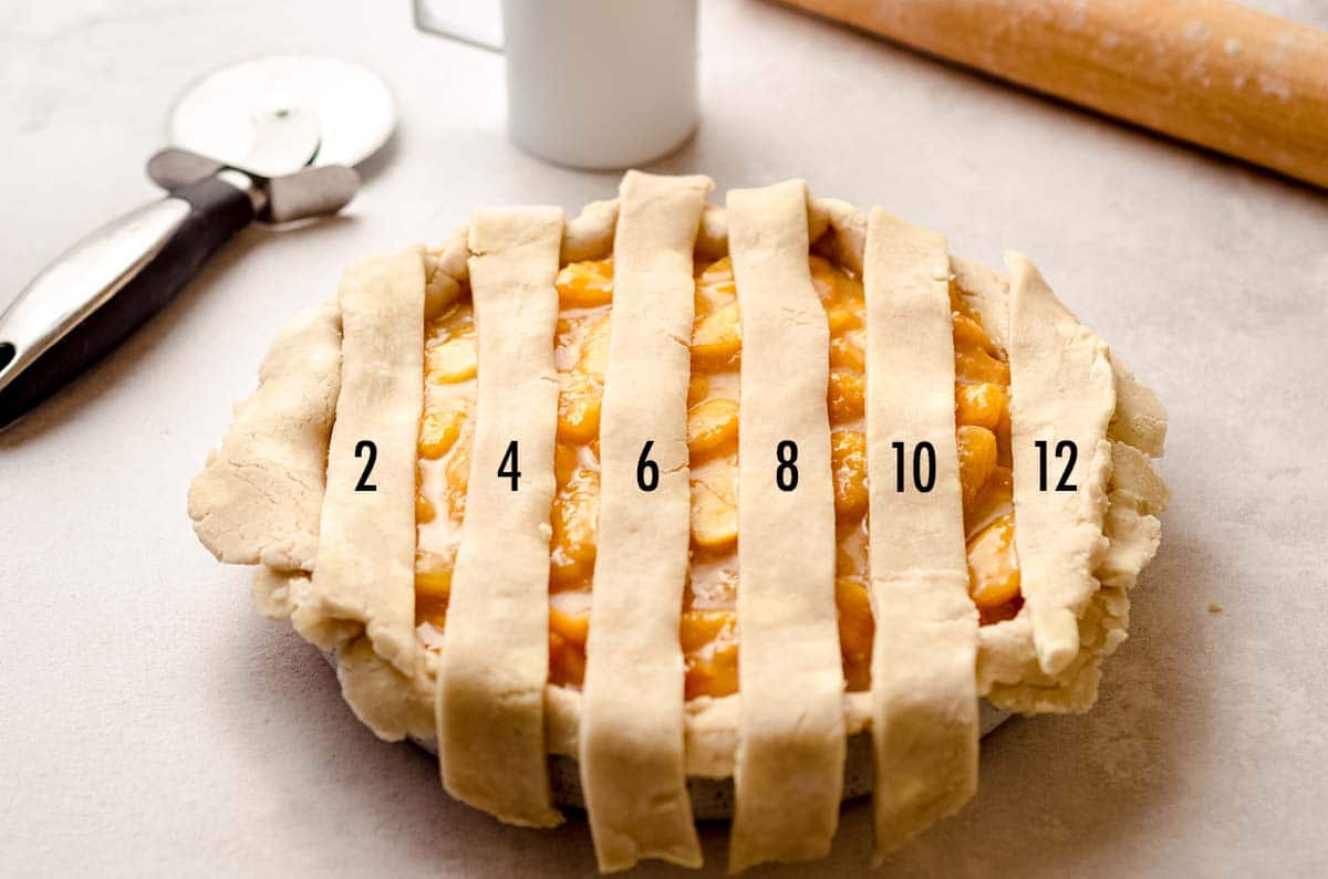 Laying every second strip of pie dough on top of a filled pie.