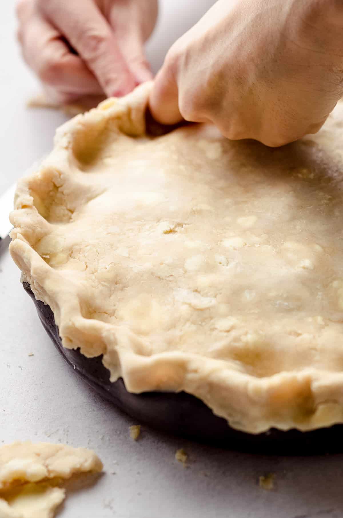 fingers crimping a top crust of an apple pie dessert