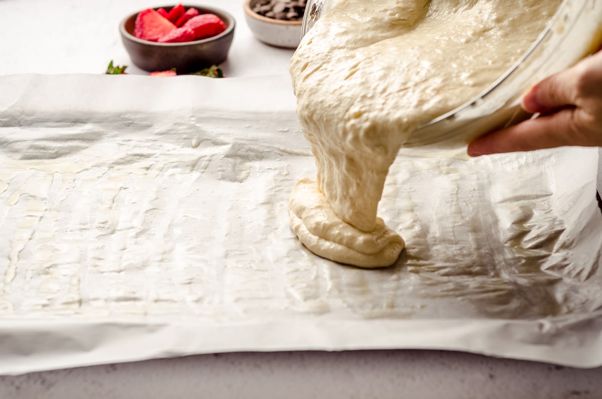 pouring pancake batter into a large baking sheet lined with parchment