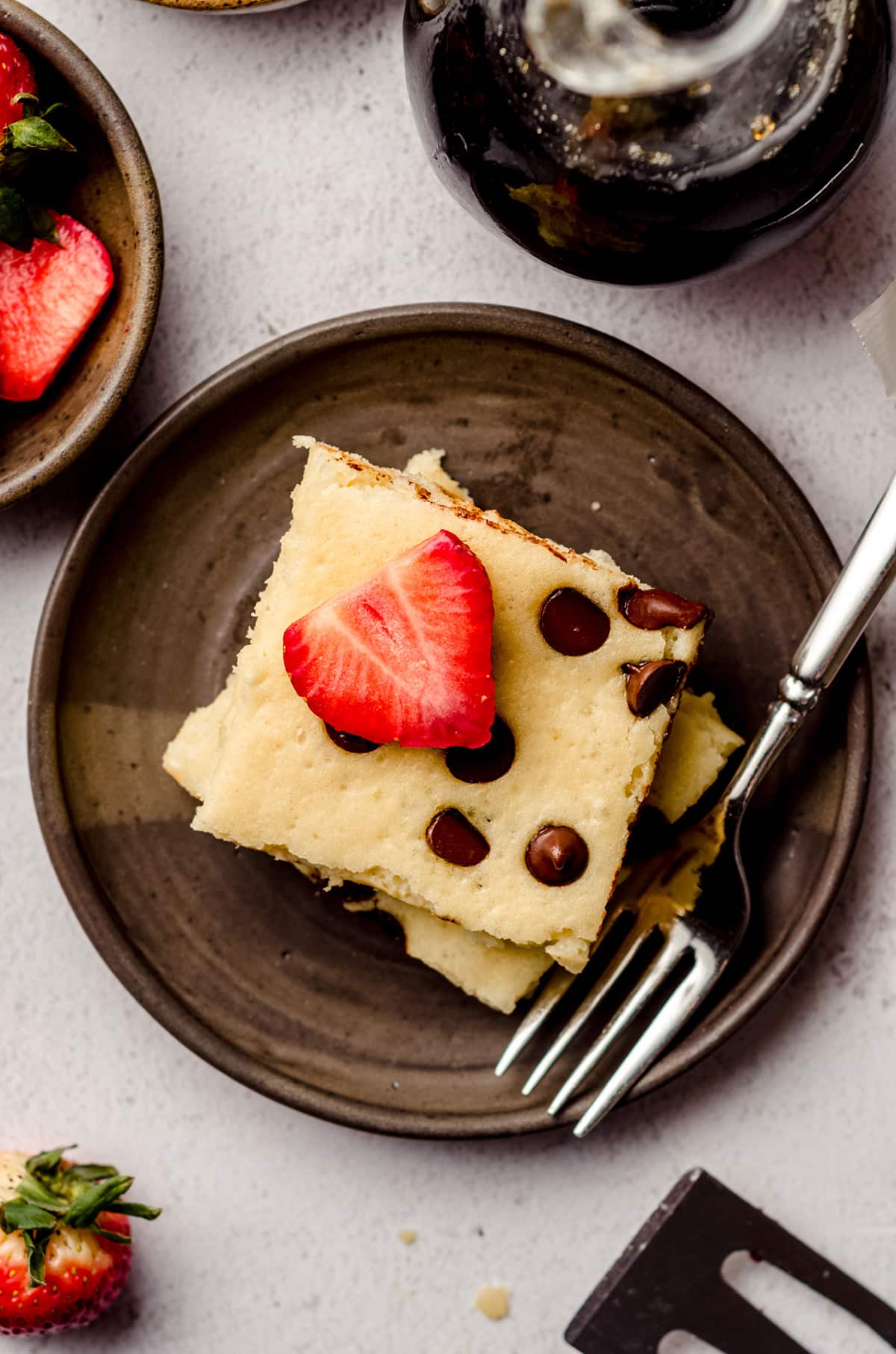 aerial photo of chocolate chip sheet pan pancakes on a plate with sliced strawberry and a fork