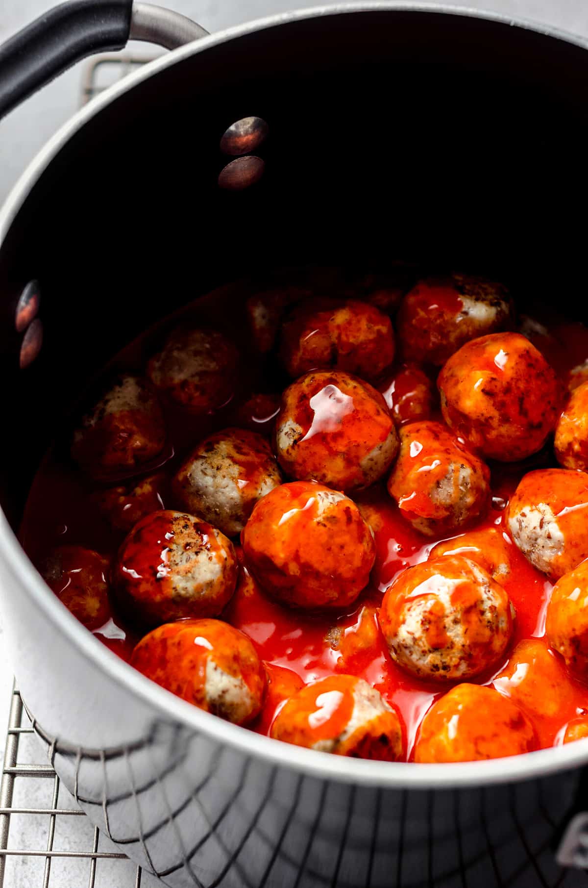 Meatballs tossed with buffalo sauce in a saucepan.