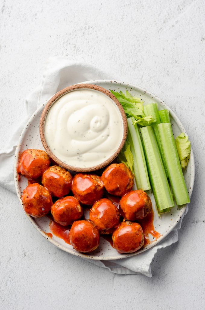 A plate with buffalo sauce coated meatballs, celery, and a creamy dressing.