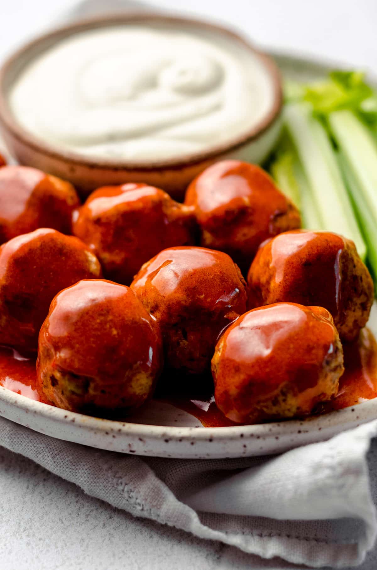 Buffalo coated meatballs on a plate, with celery on the side.