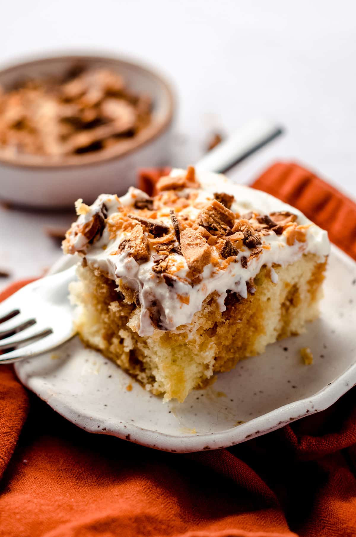 A square of cake covered in homemade whipped cream and crushed candy bars.