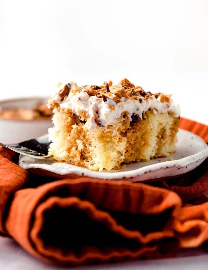 A square of poke cake on a plate, topped with crushed butterfingers.